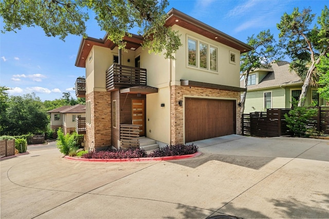 view of front of property with a garage, concrete driveway, a balcony, stone siding, and stucco siding