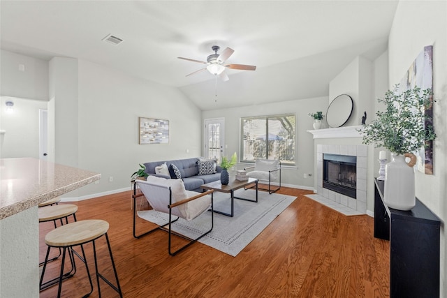 living room featuring visible vents, a tile fireplace, ceiling fan, wood finished floors, and vaulted ceiling