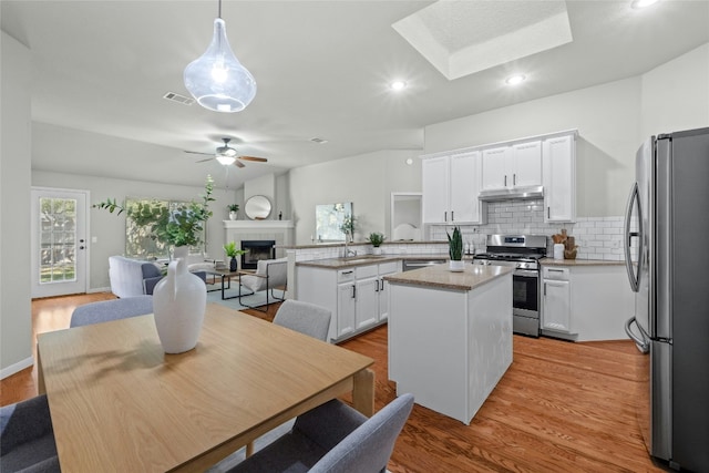 kitchen with visible vents, appliances with stainless steel finishes, open floor plan, under cabinet range hood, and a fireplace