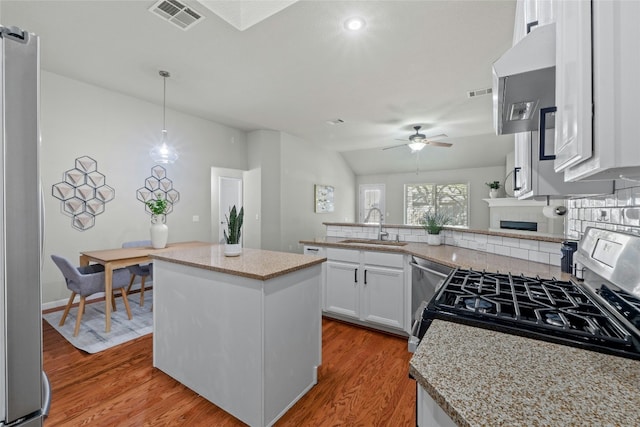 kitchen with light wood-style flooring, a peninsula, a sink, visible vents, and freestanding refrigerator