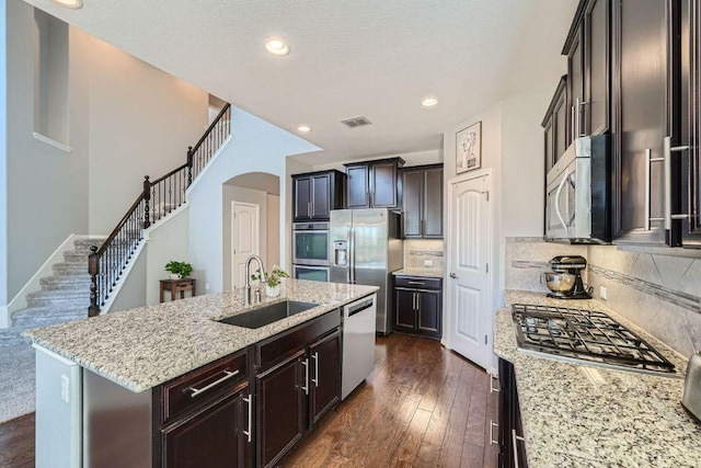 kitchen featuring visible vents, dark wood-type flooring, a kitchen island with sink, stainless steel appliances, and a sink