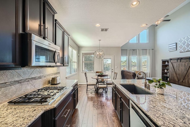 kitchen featuring decorative backsplash, appliances with stainless steel finishes, dark wood-type flooring, a sink, and light stone countertops