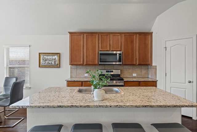 kitchen with appliances with stainless steel finishes, brown cabinetry, backsplash, and a breakfast bar