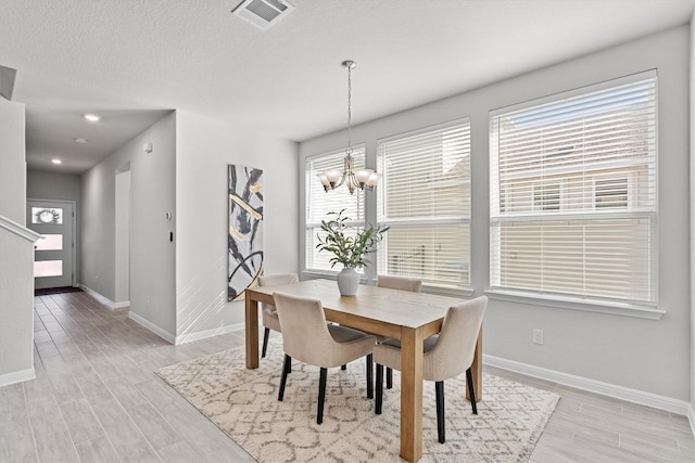 dining space featuring a textured ceiling, a notable chandelier, visible vents, baseboards, and light wood-style floors