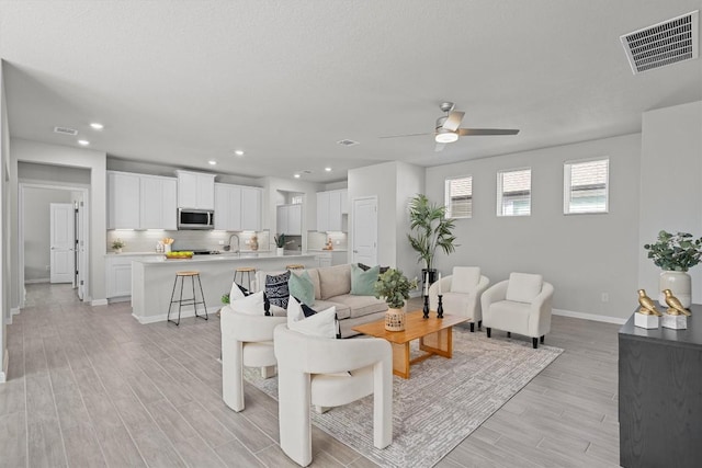 living area featuring baseboards, visible vents, ceiling fan, and light wood finished floors