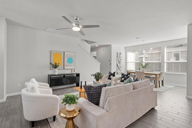 living area featuring baseboards, ceiling fan with notable chandelier, visible vents, and wood finish floors