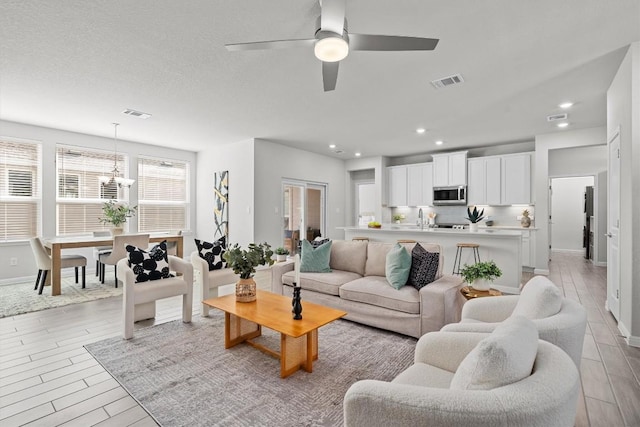 living room featuring light wood-style flooring, visible vents, and ceiling fan with notable chandelier