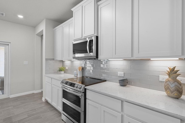 kitchen with decorative backsplash, appliances with stainless steel finishes, white cabinets, light stone countertops, and baseboards