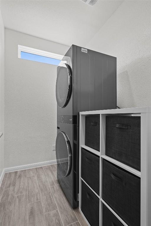 laundry room featuring laundry area, baseboards, stacked washer and dryer, and wood finished floors