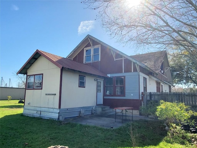 rear view of house with entry steps, metal roof, a patio, fence, and a lawn