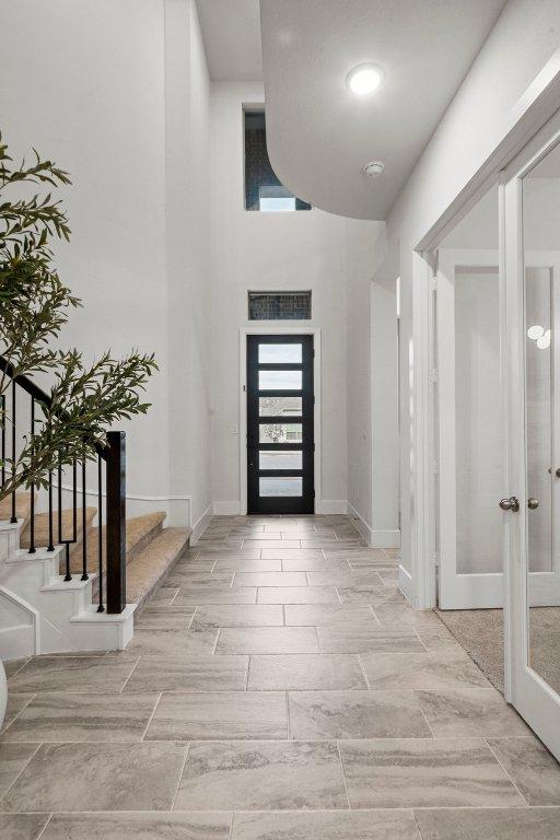 foyer entrance featuring a towering ceiling, french doors, stairway, and baseboards