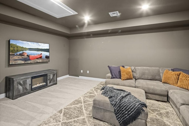 carpeted home theater featuring baseboards, visible vents, and a glass covered fireplace