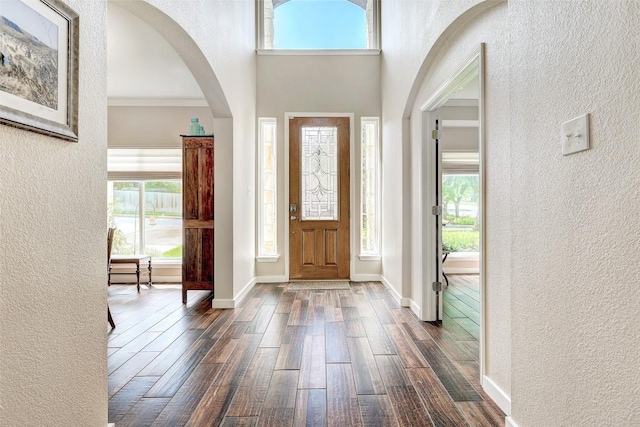 entrance foyer with dark wood-type flooring, a textured wall, and baseboards