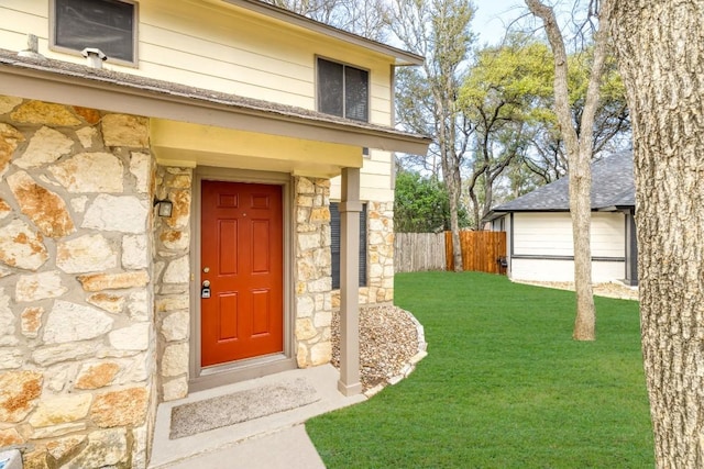 view of exterior entry featuring stone siding, fence, and a lawn