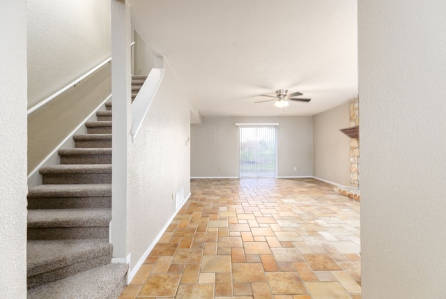 interior space with ceiling fan, visible vents, baseboards, stairs, and stone finish flooring