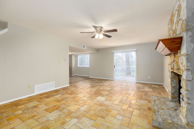 unfurnished living room featuring ceiling fan, a fireplace, visible vents, and baseboards