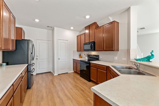 kitchen featuring brown cabinets, visible vents, light wood-style floors, a sink, and black appliances