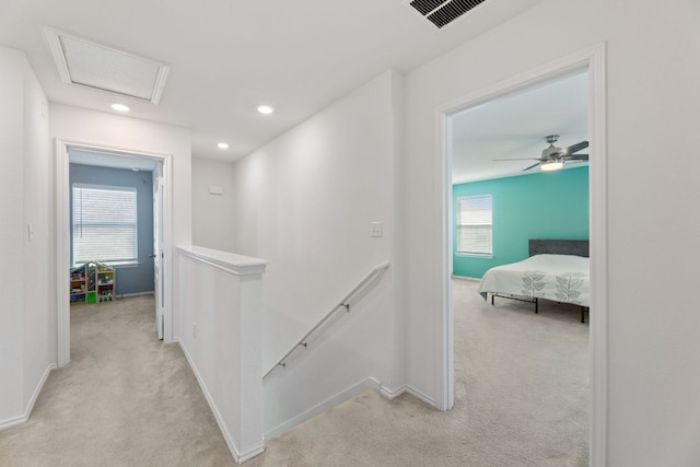 hall with visible vents, attic access, an upstairs landing, and light colored carpet