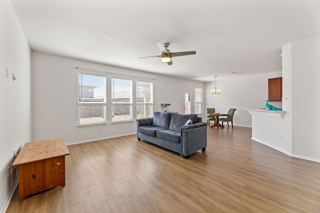 living room featuring ceiling fan with notable chandelier, light wood-style flooring, and baseboards