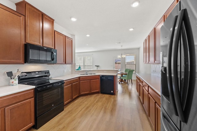 kitchen featuring light wood-style flooring, a peninsula, light countertops, black appliances, and backsplash