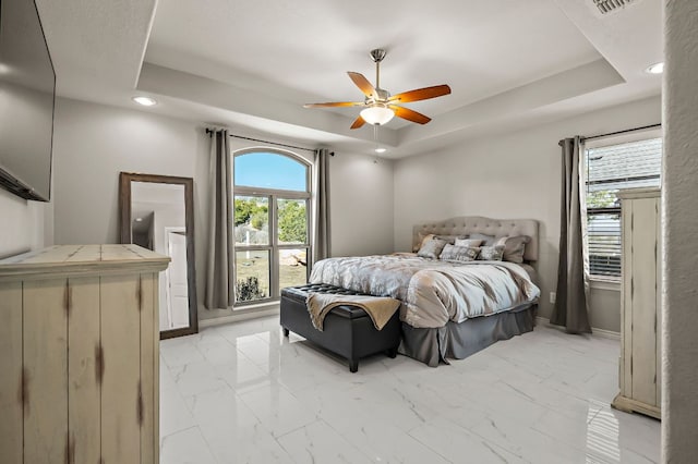 bedroom featuring marble finish floor, a tray ceiling, and multiple windows