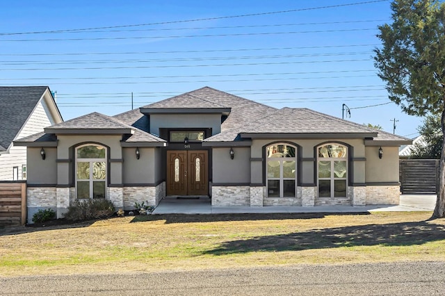 view of front of house with a front yard, stone siding, fence, and stucco siding