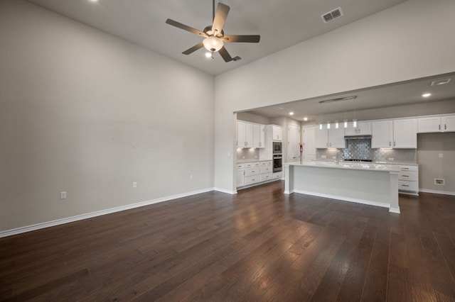 unfurnished living room with baseboards, visible vents, ceiling fan, dark wood-type flooring, and a sink