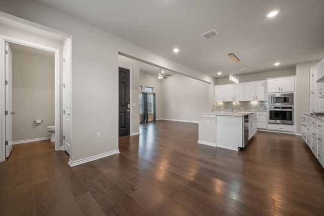 kitchen featuring dark wood-style flooring, light countertops, decorative backsplash, appliances with stainless steel finishes, and white cabinetry