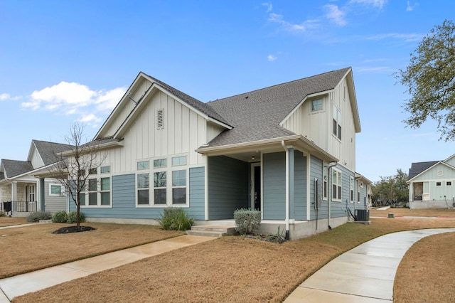 view of front of house with board and batten siding, a shingled roof, a front lawn, and central air condition unit