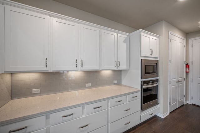 kitchen with tasteful backsplash, white cabinets, light stone counters, appliances with stainless steel finishes, and dark wood-type flooring