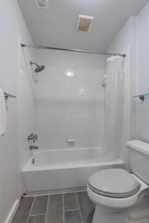 bathroom featuring toilet, wood tiled floor, visible vents, and shower / bath combo with shower curtain