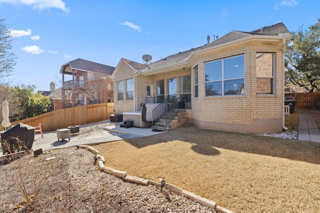 rear view of house featuring brick siding, a yard, a patio, an outdoor fire pit, and a fenced backyard