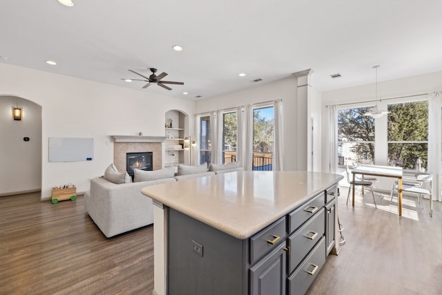 kitchen with a kitchen island, wood finished floors, gray cabinetry, a fireplace, and recessed lighting