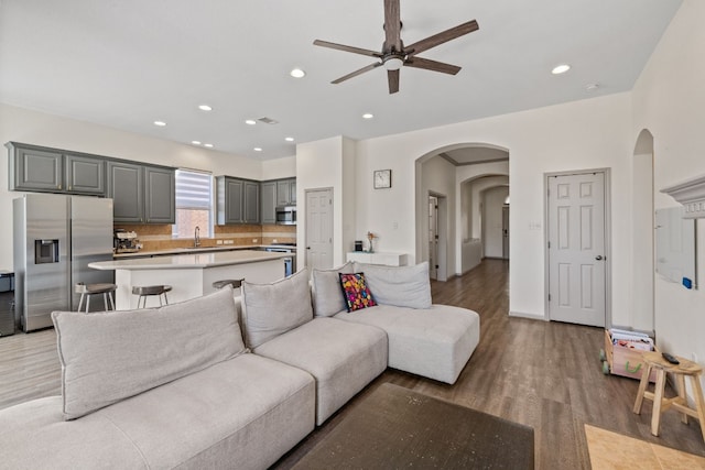 living room with light wood finished floors, ceiling fan, arched walkways, and recessed lighting