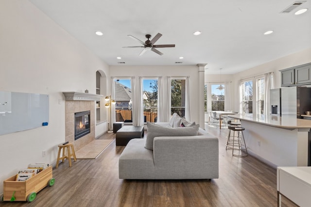 living room with a tiled fireplace, dark wood finished floors, visible vents, and recessed lighting