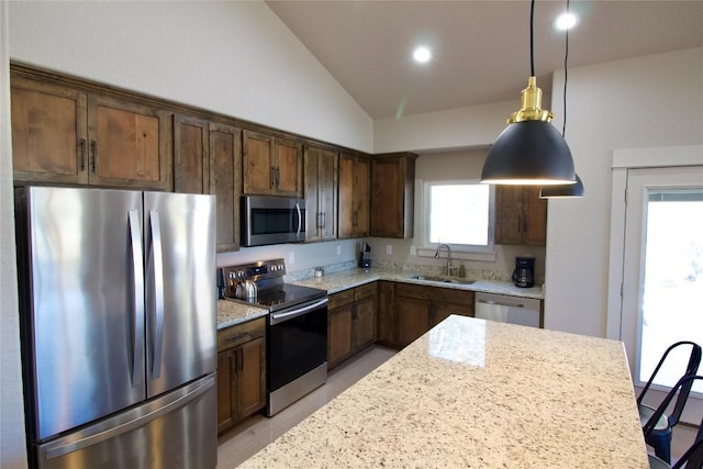 kitchen with decorative light fixtures, stainless steel appliances, vaulted ceiling, a sink, and light stone countertops