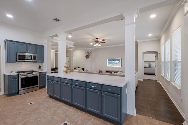 kitchen with crown molding, stainless steel appliances, open floor plan, ceiling fan, and ornate columns