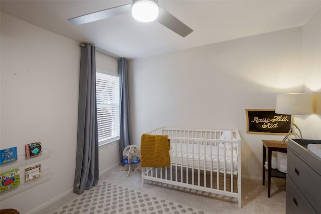 carpeted bedroom featuring a ceiling fan, a nursery area, and baseboards