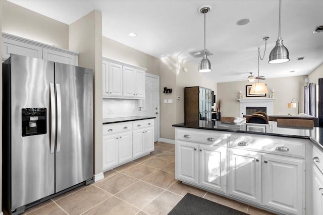 kitchen with white cabinets, decorative backsplash, dark countertops, a lit fireplace, and stainless steel refrigerator with ice dispenser