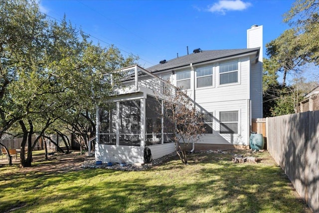 back of house featuring a sunroom, a chimney, fence, and a lawn