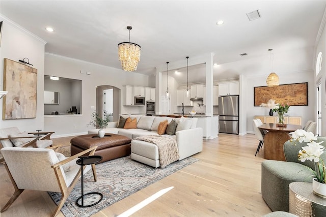 living area with light wood finished floors, visible vents, arched walkways, crown molding, and a notable chandelier