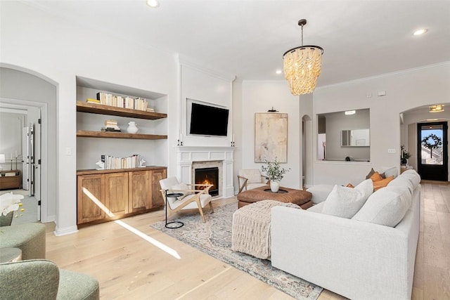 living room with light wood-style floors, a warm lit fireplace, built in features, and crown molding