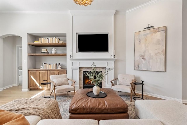 living area featuring arched walkways, a warm lit fireplace, light wood-style floors, built in features, and ornamental molding