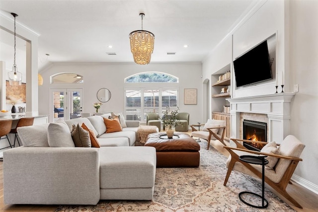 living room featuring a warm lit fireplace, built in shelves, wood finished floors, visible vents, and ornamental molding