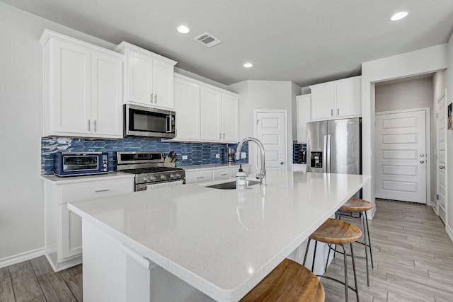 kitchen with a toaster, stainless steel appliances, decorative backsplash, a sink, and a large island with sink