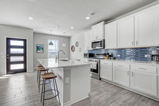 kitchen with stainless steel appliances, wood finish floors, a sink, and an island with sink