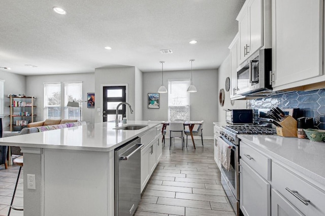 kitchen with a breakfast bar, a sink, appliances with stainless steel finishes, decorative backsplash, and a center island with sink