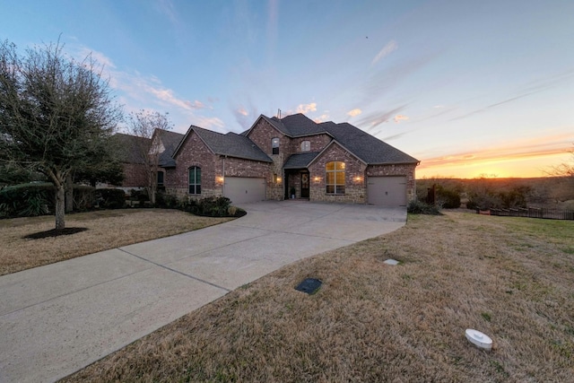 french country inspired facade with driveway, stone siding, an attached garage, a front lawn, and brick siding