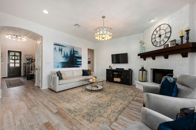 living area with arched walkways, a fireplace, visible vents, light wood-style flooring, and an inviting chandelier