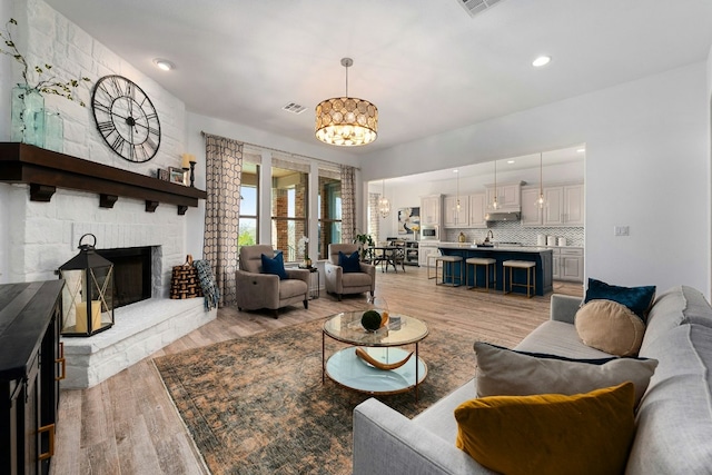 living area with a chandelier, a stone fireplace, light wood-style flooring, and visible vents